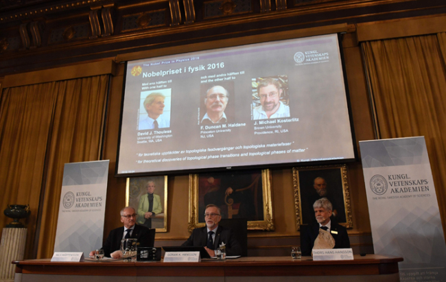 (L-R) The acting chairman of the Nobel Committee for Physics Nils Martensson, the Permanent Secretary of the Royal Swedish Academy of Sciences Goran K Hansson and Thors Hans Hansson, member of the Nobel Committee for Physics sit in front of a screen displaying the winners of the Nobel Prize in Physics (L-R) David J Thouless, F Duncan M Haldane and J Michael Kosterlitz during a press conference to announce the winner of the 2016 Nobel Prize in Physics at the Royal Swedish Academy of Sciences in Stockholm on October 4, 2016. David J. Thouless, F. Duncan M. Haldane and J. Michael Kosterlitz were awarded the 2016 Nobel Physics Prize "for theoretical discoveries of topological phase transitions and topological phases of matter". / AFP PHOTO / JONATHAN NACKSTRAND/ 